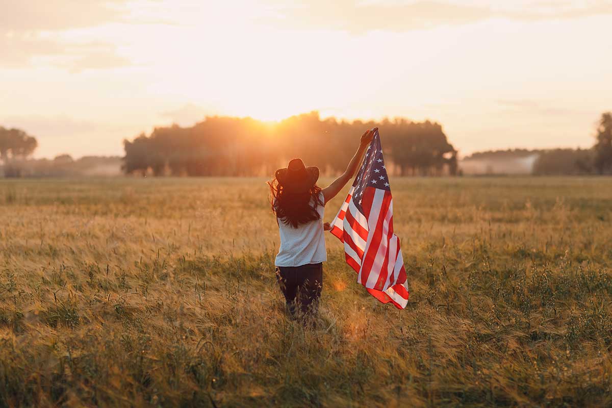 cowgirl holding an American flag toward the sunset